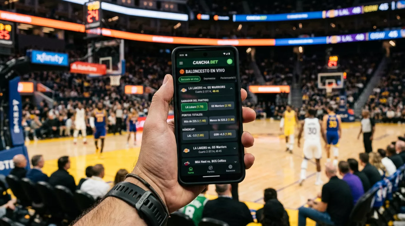 Mano sosteniendo un teléfono móvil con una app de apuestas deportivas en un pabellón de baloncesto